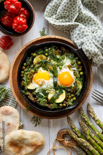 Green shakshuka with green vegetables and eggs in cast iron skillet, top view