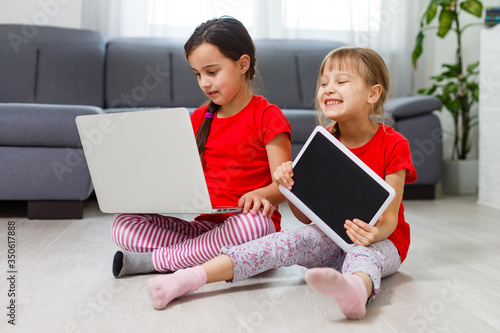 Two little girls are playing with laptop in playroom at home