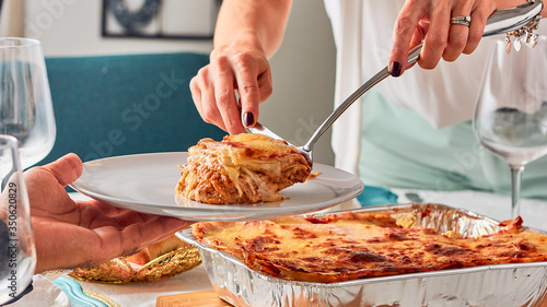 woman serving portion of lasagna food on a family table. Traditional Italian food