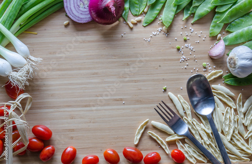 Cherry tomatoes, onions, Italian pasta, green beans, spoon, fork, arranged in a circle on a bamboo sheet. Healthy ingredients in the atlas. Kitchen composition before cooking, preparation.