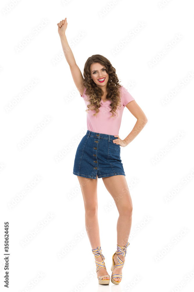 Happy Woman In Jeans Mini Skirt And Wedge Shoes Is Standing With Arm Raised And Cheering