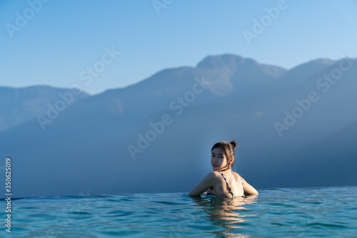Sexy woman relaxing in infinity swimming pool with stunning mountain view at luxurious resort / vacation concept