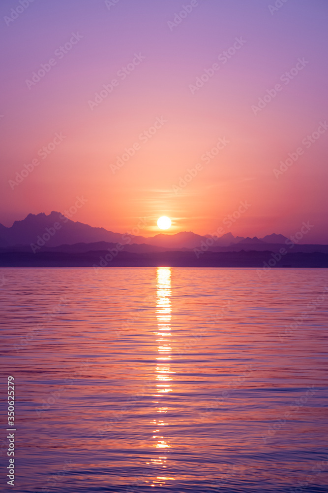 Stunning seascape on beautiful colorful sunset. The sun hides in the mountains and reflected in calm sea water. Red, pink and orange sky. Meditation. No people. Sun line. Romantic journey.