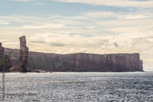 ocean view of Old Man of Hoy, a tall sandstone stack at the coast between Stromness and Scrabster at Orknay in Scotland, Uk. Famous British climbing place at cliffs with stunning clouds in the sky photo