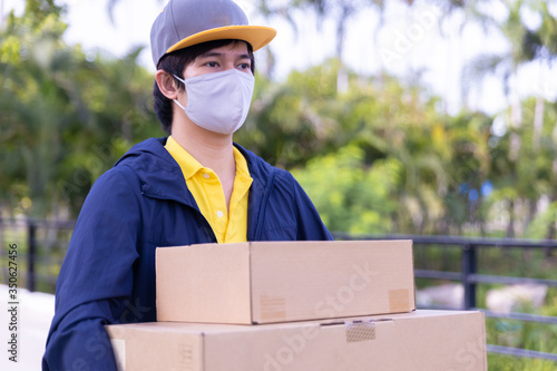Delivery man employee wearing a face mask and holding boxes outside.
