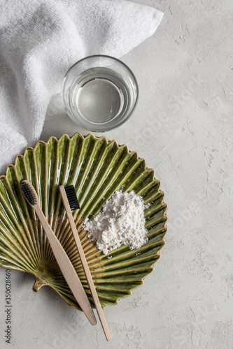 Two bamboo toothbrushes on a beautiful plate with a towel and a glass of water on a gray background, top view. Zero West. Morning routines, self-care photo