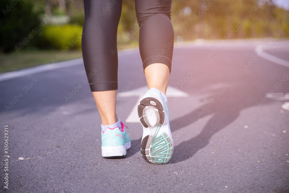 Runner athlete feet running on road under sunlight in the morning.