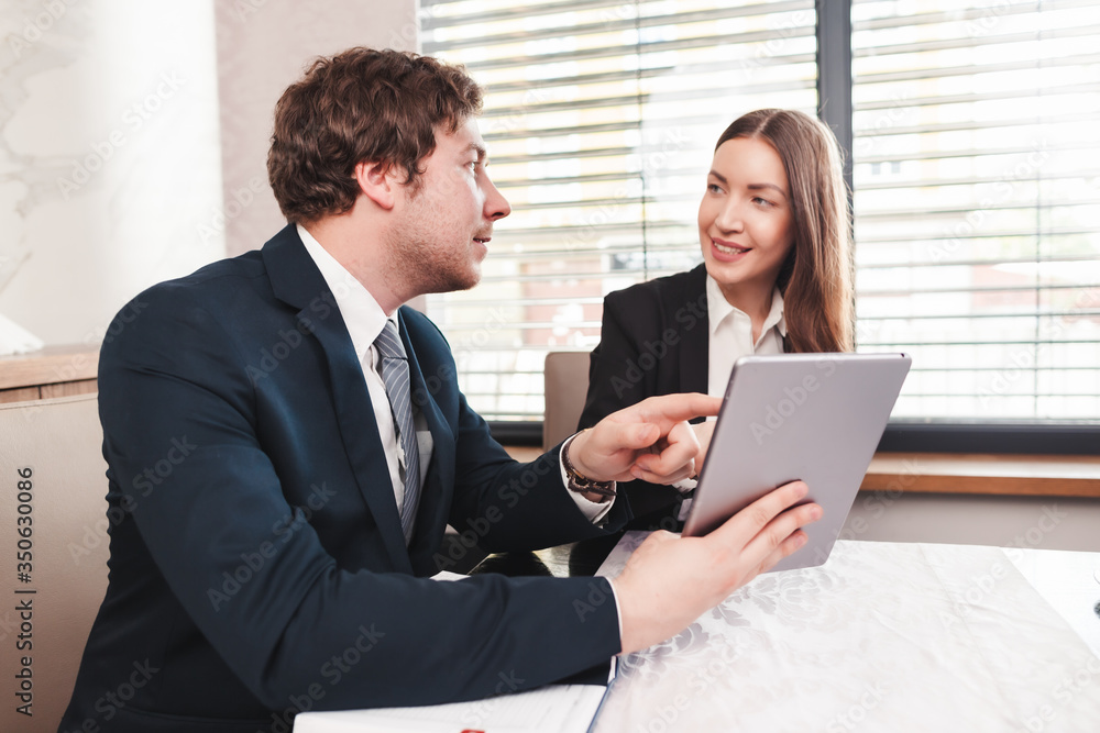 Young business woman and businessman are using tablet and document, talking about finances. Young business woman and businessman are using tablet and document, talking about finances.