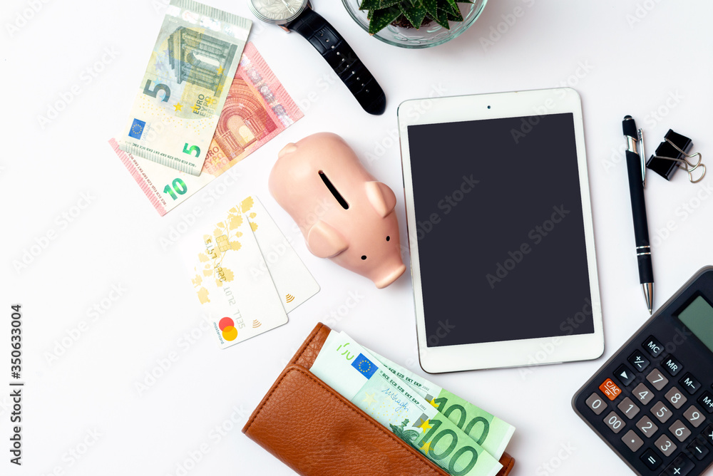 Top view image.Piggy bank, office supplies,pen, credit cards,calculator, clock and money on a white desk. Top view image.Piggy bank, office supplies,pen, credit cards,calculator, clock and money on a white desk.