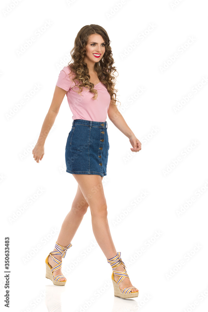 Naklejka premium Cute Woman In Jeans Mini Skirt And Wedge Shoes Is Walking And Looking Away