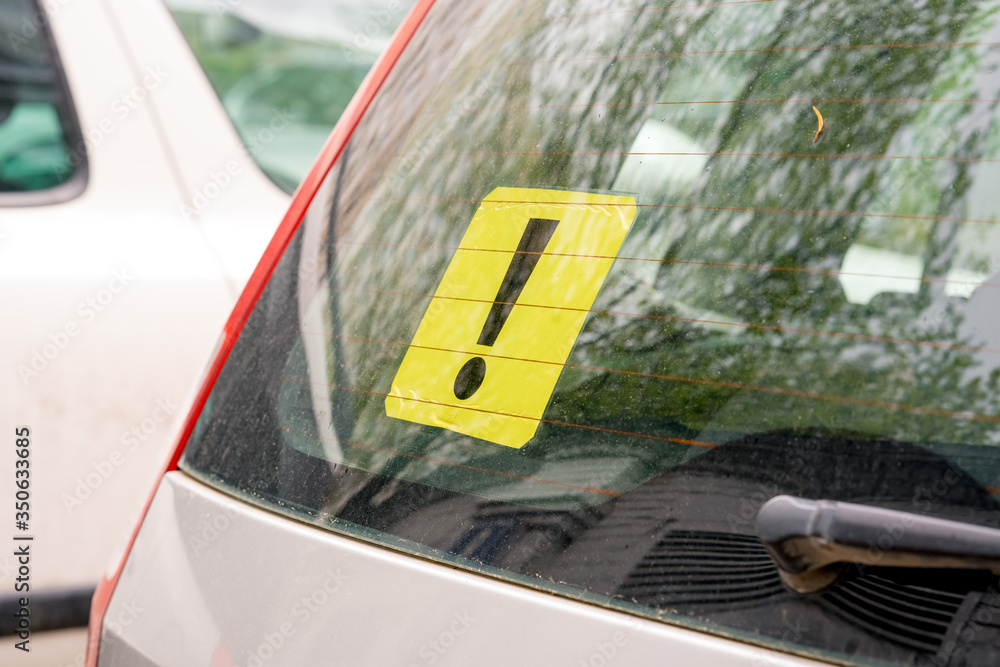 A yellow exclamation mark on the rear window of a car. Inexperienced