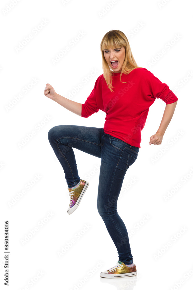 The Woman Stands On One Leg With A Raised Fist And Shoutes The Woman Stands On One Leg With A Raised Fist And Shoutes