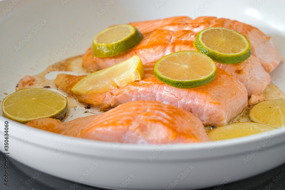 Bio Lachsfilet auf der Haut gebraten in einer weißen Pfanne mit Zitronen- und Limettenscheiben Bio Lachsfilet auf der Haut gebraten in einer weißen Pfanne mit Zitronen- und Limettenscheiben