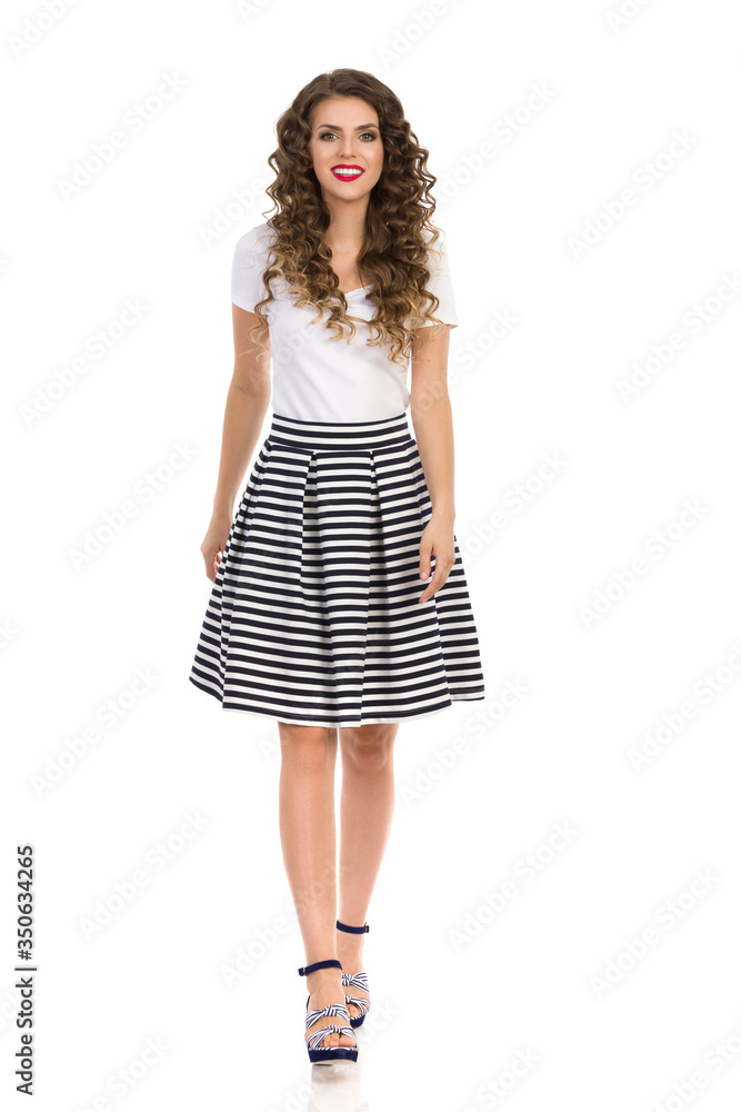 Young Woman In Striped Skirt And High Heels Is Walking Towards Camera. Front View. Young Woman In Striped Skirt And High Heels Is Walking Towards Camera. Front View.
