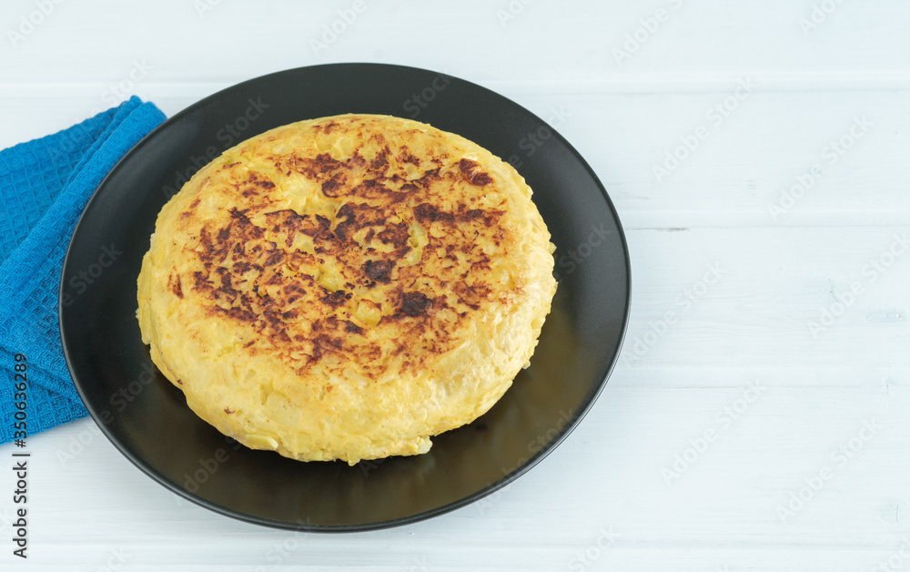 Potato omelette on a black plate on a white background. Copy space.