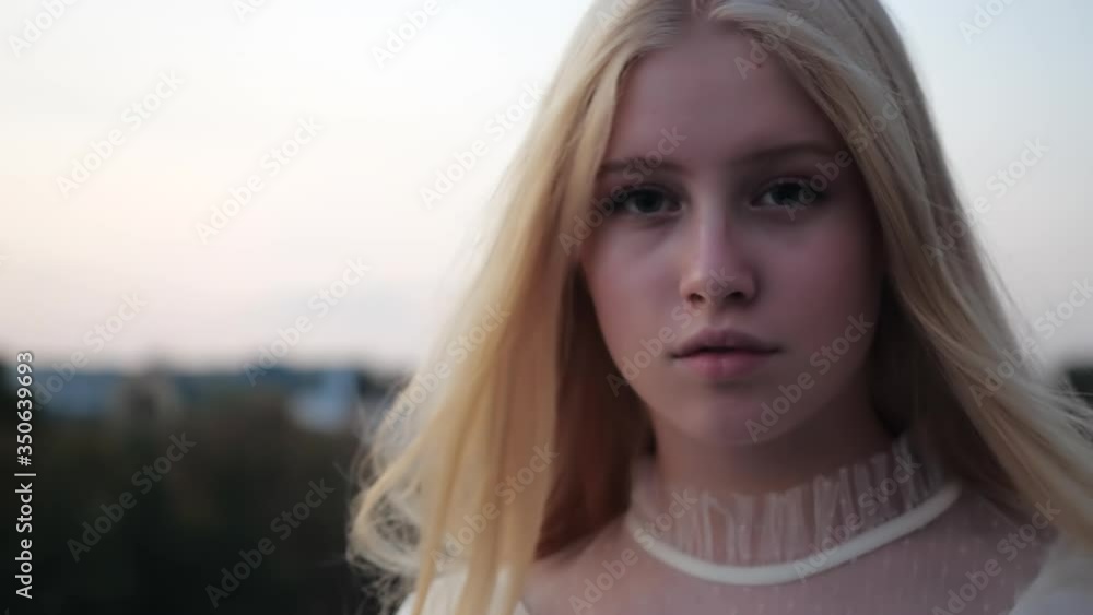 Close-up front view of pretty face of a charming caucasian female model walking forward towards the camera. Beautiful blonde confidently and briskly strolling through the dying city, Kharkov, Ukraine.