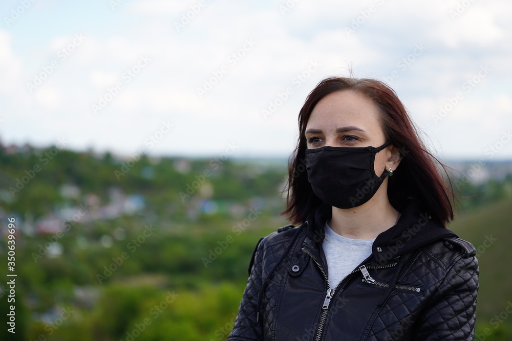 Young woman in black medical mask and leather jacket on hill on cloudy day. Adult female walking alone in countryside. Young woman in black medical mask and leather jacket on hill on cloudy day. Adult female walking alone in countryside.