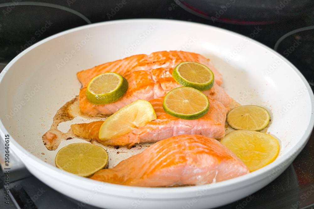 Bio Lachsfilet auf der Haut gebraten in einer weißen Pfanne mit Zitronen- und Limettenscheiben Bio Lachsfilet auf der Haut gebraten in einer weißen Pfanne mit Zitronen- und Limettenscheiben