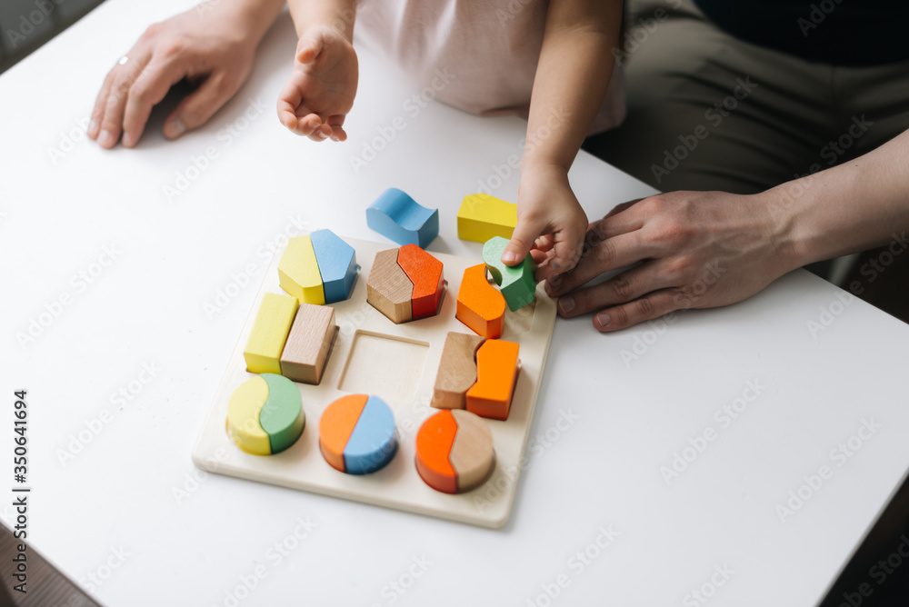 Close-up of hands of unrecognizable father and him daughter playing together with colorful wooden block toys at table. Close-up of hands of unrecognizable father and him daughter playing together with colorful wooden block toys at table.
