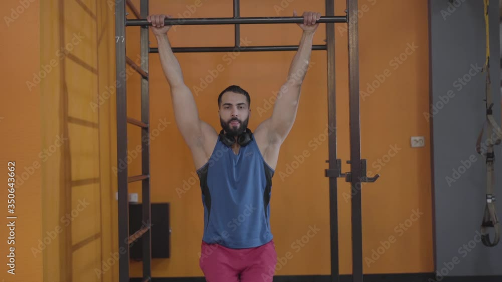 Workout of handsome young Middle Eastern man in gym. Strong bearded sportsman hanging on bars and lifting legs. Sports club, hanging leg raises, fitness, healthy lifestyle. Workout of handsome young Middle Eastern man in gym. Strong bearded sportsman hanging on bars and lifting legs. Sports club, hanging leg raises, fitness, healthy lifestyle.