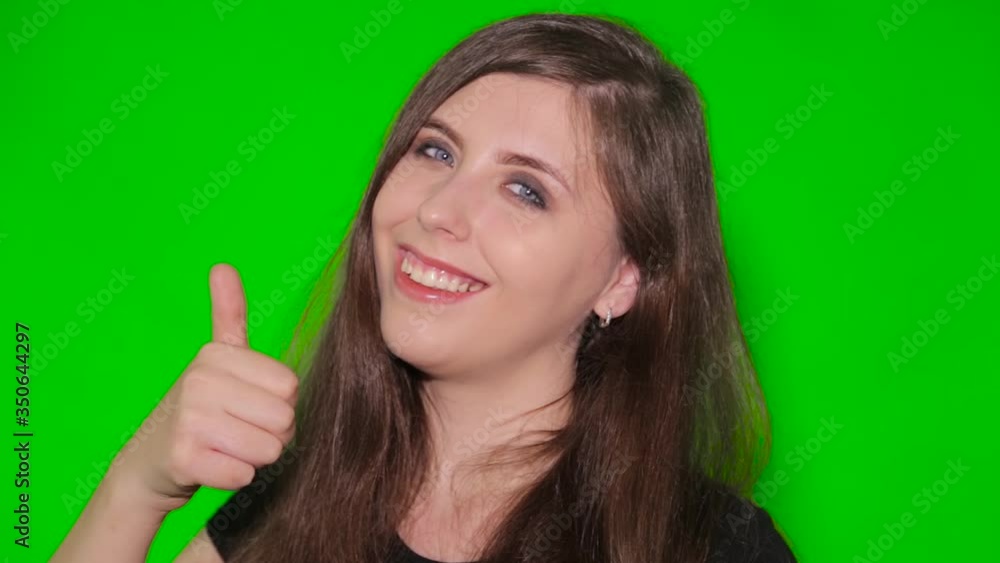 Girl shows a gesture thumb up isolated on a green screen. Close-up face of a young smiling woman on chromakey background. Girl shows a gesture thumb up isolated on a green screen. Close-up face of a young smiling woman on chromakey background.