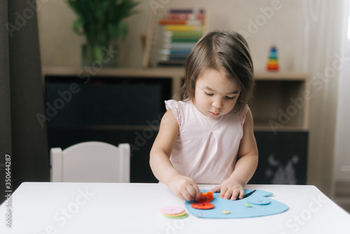 Cute beautiful little two-year-old girl is playing with educational toy standing at the table in cozy children room.