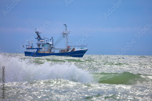blue fishing boat in the north sea at blue sky and waves