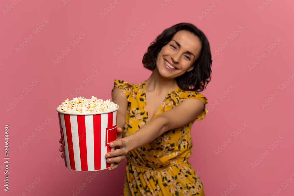 Here is your snack. Close-up photo of a young sweet girl in a floral dress, who is looking in the camera and holding a tube of popcorn in her hands. Here is your snack. Close-up photo of a young sweet girl in a floral dress, who is looking in the camera and holding a tube of popcorn in her hands.