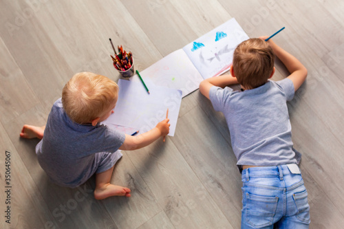 Two little boys drawing on the floor in his room