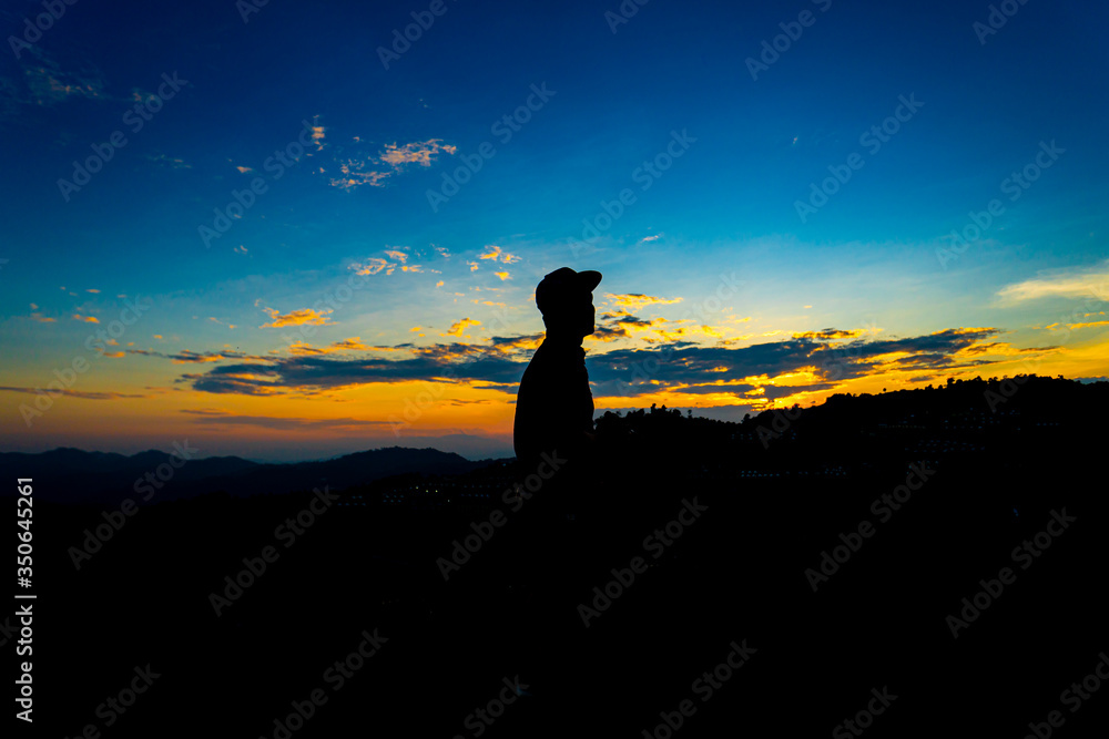 Silhouette Man Standing on Hill with  Cap at the Sunset on Mountain with Blue Sky. Enjoying Peaceful Moment Concept.
