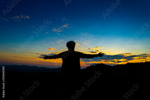 Silhouette Happy Man Standing on Hill at the Sunset on Mountain with Blue Sky. Enjoying Peaceful Moment Concept. Relaxing or achievement Concept.