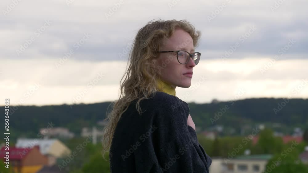 Young woman wearing robe stands in balcony and admires morning view. Cold weather Young woman wearing robe stands in balcony and admires morning view. Cold weather