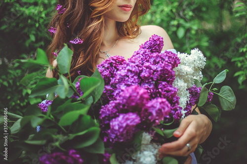 A young girl with a large bouquet of purple lilac. A girl in a Park among green trees.Beautiful spring flowers.