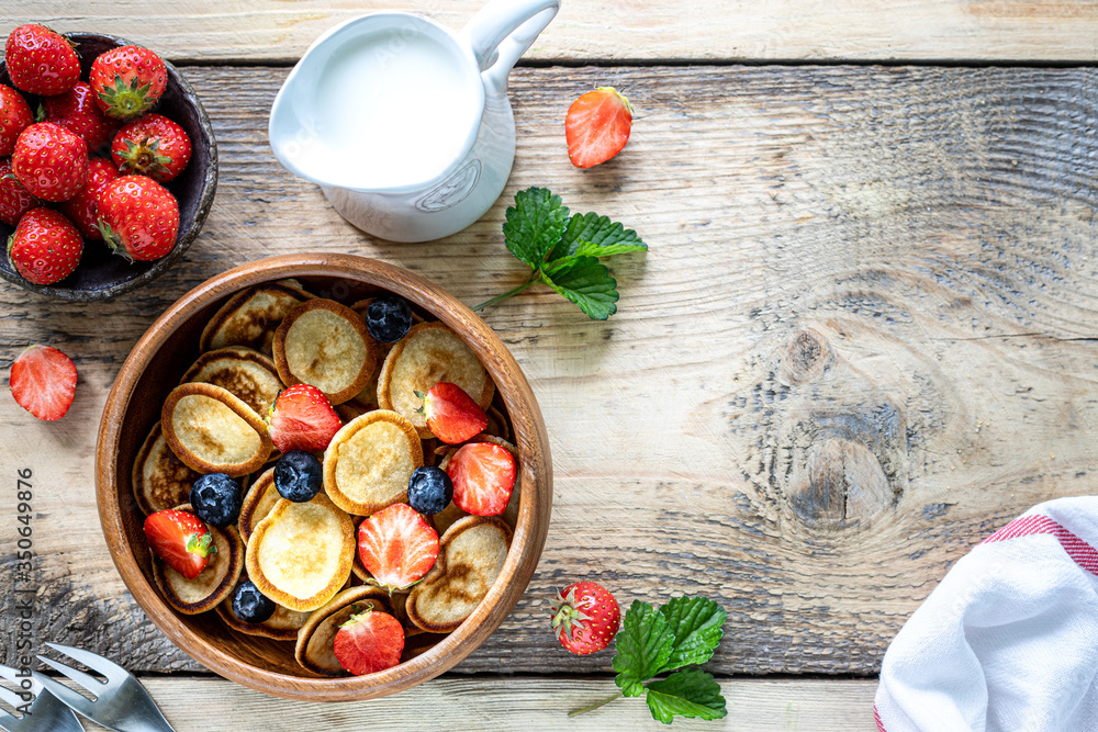 Tiny pancake cereal and chocolate mini pancakes in a wooden bowl with honey and strawberries on a wooden background. Top view. Copy space. Trendy food