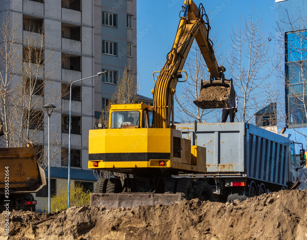 Excavator loader and dump truck during earthworks at a construction site. Loading land in the back of a heavy truck. Excavator digs land for the construction of a new park area. Excavator loader and dump truck during earthworks at a construction site. Loading land in the back of a heavy truck. Excavator digs land for the construction of a new park area.
