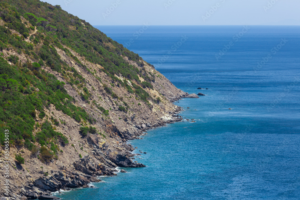 Coastline with cliff mountain and seashore view. Pitched rock face on the sea. Elba island in Italy. Aerial view. Green vegetation.