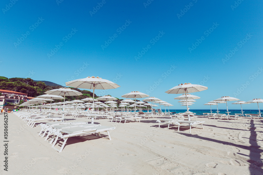 Beach and Italian Tyrrhenian coast with a multitude seamsless of beach umbrellas, deckchairs for vacationers. Trees and nature in the background.