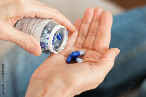 Female hand close up holding a medicine, elderly woman hands with pill on spilling pills out of bottle .