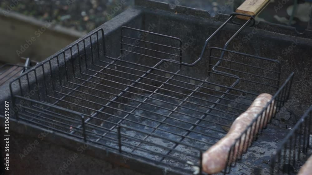 The man puts still-prepared sausages on the grill. Grilled sausages in a natural shell. Hand close-up. The man puts still-prepared sausages on the grill. Grilled sausages in a natural shell. Hand close-up.