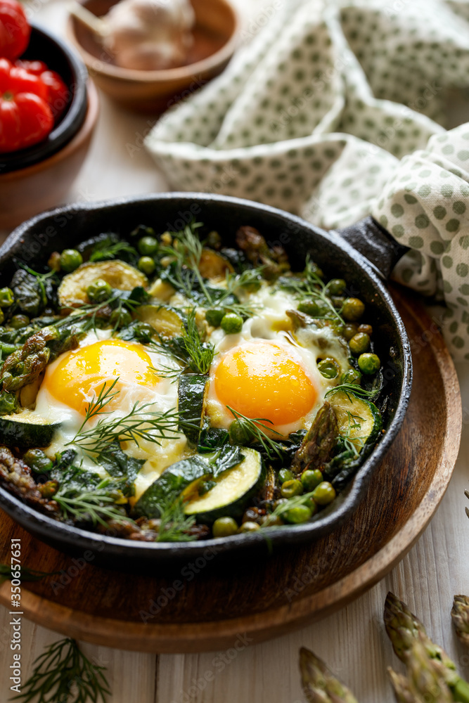 Green shakshuka with green vegetables and fried eggs in cast iron skillet on a white wooden table close up view