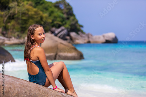 A child, a girl in a bathing suit sitting on a rock near the water