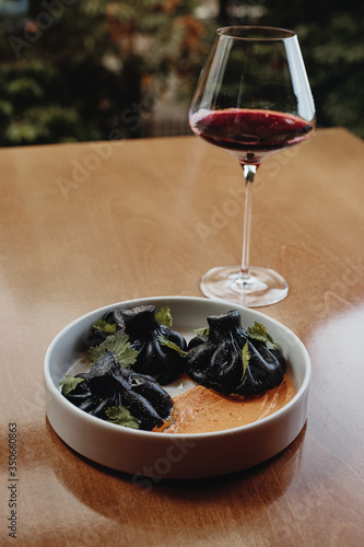 black Georgian khinkali in plate from the restaurant with cream on wooden table against the background of glass of wine