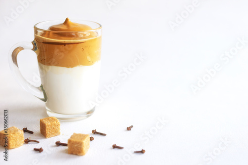 Trendy delicious Korean drink. Dalgona coffee. Whipped instant coffee with milk in a tall glass on a white background, pieces of cane sugar. Horizontal, copy space