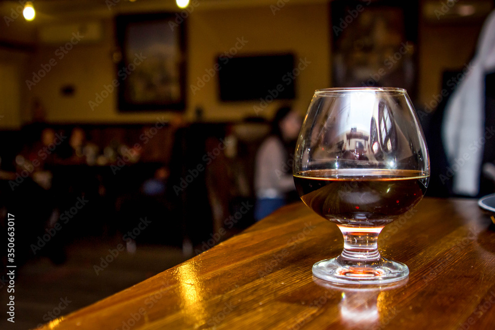 A glass of cognac stands at the bar, against the backdrop of visitors to the cafe