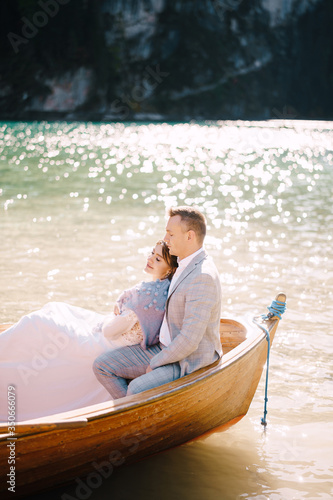 A wedding couple is sitting in a wooden boat on the Lago di Braies in Italy. Newlyweds in Europe  on Braies lake  in the Dolomites. The groom hugs the bride.