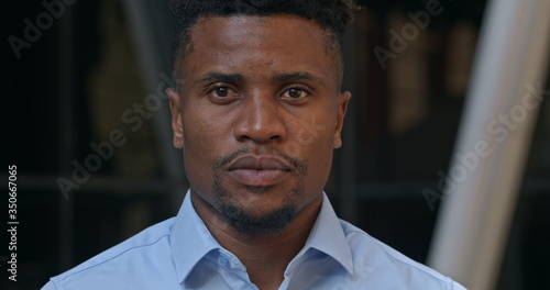 Close up view of serious good looking businessman in shirt looking to camera. Portrait of successful afro american guy in middle 30s office manager or team boss. Outdoors. © oleg_kozytskyi