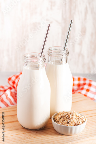 Non dairy oat milk in glass bottles with reusable metal straws. Healthy vegan milk alternative still life, copy space. Substitute for traditional cow milk with oat flakes, healthy lifestyle concept