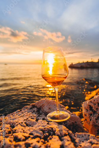 glass of wine at rocky sea beach on sunset