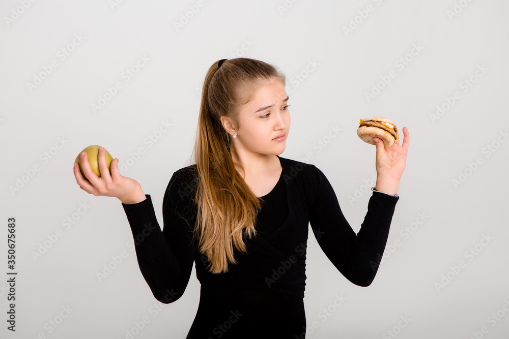 young slender girl holds a hamburger and an apple against a white background. choosing healthy food, no fast food, space for text young slender girl holds a hamburger and an apple against a white background. choosing healthy food, no fast food, space for text