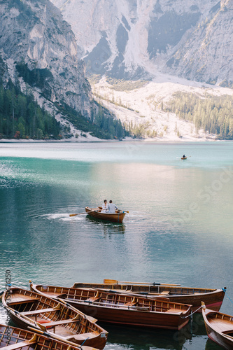 Wedding couple sailing in a wooden boat at the Lago di Braies in Italy. Newlyweds in Europe, on Braies lake, in the Dolomites. The groom rows the oars, the bride sits opposite him. © Nadtochiy